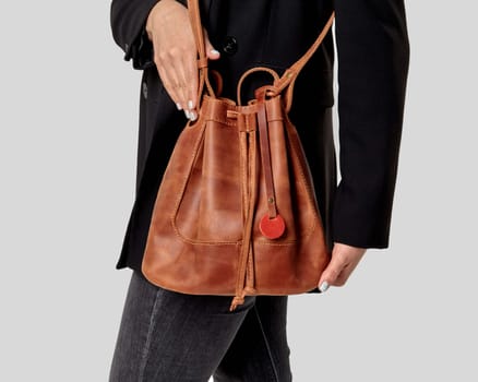 Comfortable copper-colored leather bucket bag with motivational slogan on label, drawstrings and long handle complementing stylish look of young woman in casual black jacket