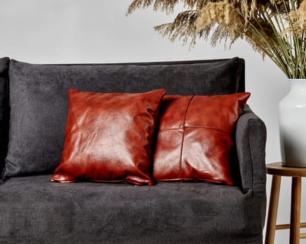 Glossy brown leather pillows adding splash of color to dark grey sofa, enhancing decor of modern living space. Stylish artisanal piece of furniture