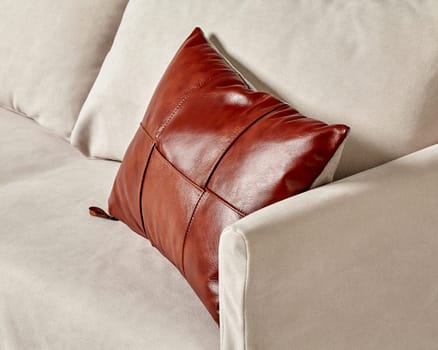 Stylish handcrafted cushion featuring glossy brown leather patchwork top creating striking contrast with light grey fabric upholstery of sofa, perfect for minimalist interior decor