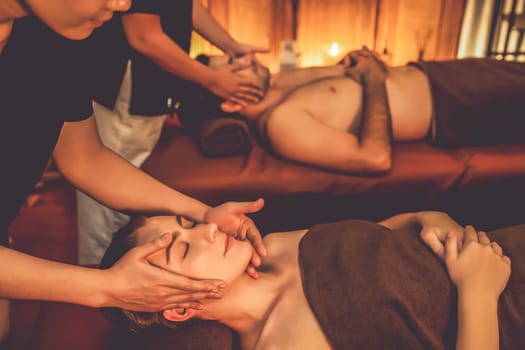 Couple customer enjoying relaxing anti-stress head massage and pampering facial beauty skin recreation leisure in warm candle lighting ambient salon spa in luxury resort or hotel. Quiescent