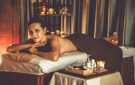 Caucasian woman customer enjoying relaxing anti-stress spa massage and pampering with beauty skin recreation leisure in warm candle lighting ambient salon spa at luxury resort or hotel. Quiescent