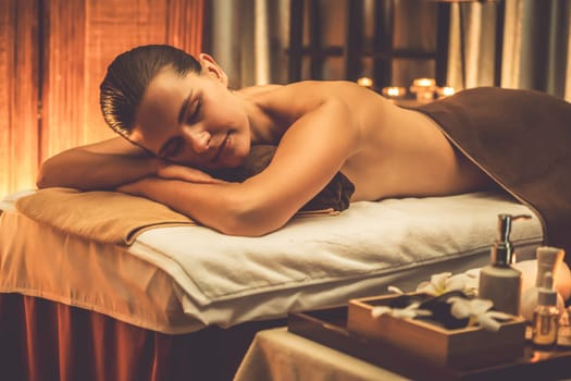 Caucasian woman customer enjoying relaxing anti-stress spa massage and pampering with beauty skin recreation leisure in warm candle lighting ambient salon spa at luxury resort or hotel. Quiescent