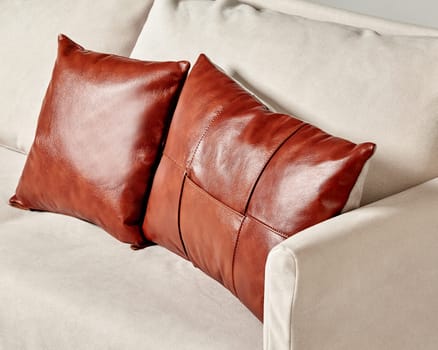 High-quality brown leather pillows harmoniously complementing modern light-grey sofa with soft fabric upholstery in chic living room interior
