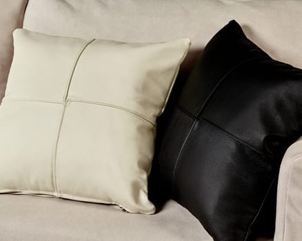 Elegantly contrasting, creamy white and deep black leather cushions resting side by side on soft sofa with beige fabric upholstery. Handcrafted items for stylish interior design
