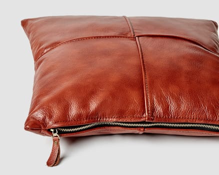 Closeup of handcrafted sofa cushion made from glossy genuine copper colored leather with neat decorative stitching and gold side zipper on white background. Stylish luxury accents for interior design