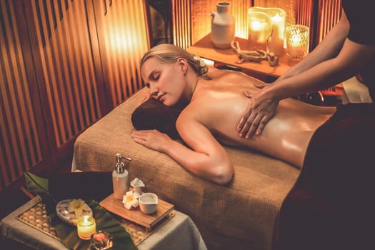 Caucasian woman customer enjoying relaxing anti-stress spa massage and pampering with beauty skin recreation leisure in warm candle lighting ambient salon spa at luxury resort or hotel. Quiescent