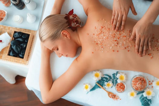 Panorama top view woman customer having exfoliation treatment in luxury spa salon with warmth candle light ambient. Salt scrub beauty treatment in health spa body scrub. Quiescent