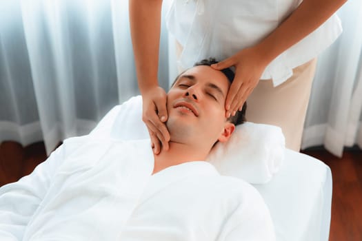 Caucasian man enjoying relaxing anti-stress head massage and pampering facial beauty skin recreation leisure in dayspa modern light ambient at luxury resort or hotel spa salon. Quiescent