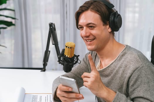 Host channel in smart broadcaster with talking show on live social media streaming using smartphone to chat with listener, wearing headphones to record video streamer at modern home studio. Pecuniary.