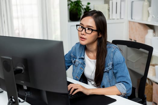 Working young beautiful asian creative manager with glasses typing to search on pc with new website design on social media online planning with blue jeans shirt at modern home office. Stratagem.