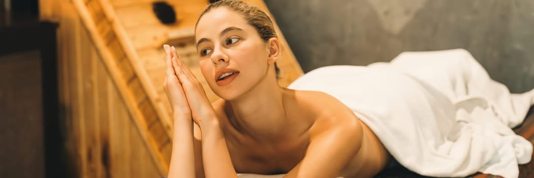 Portrait of beautiful caucasian woman in white towel woman lies on spa bed in front of warm wooden sauna cabinet with relaxation and peaceful at spa salon. Close up. A Side view. Tranquility.