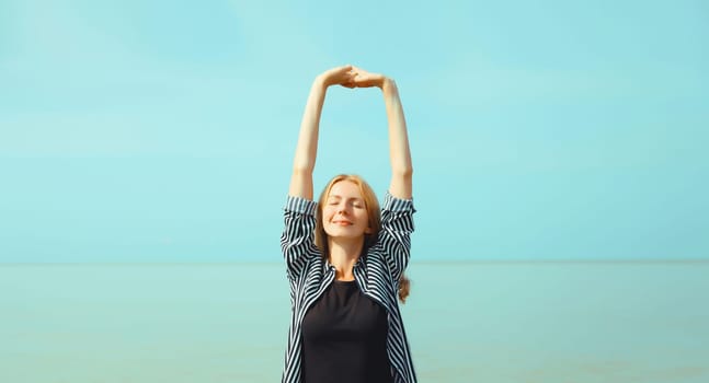 Summer vacation, happy relaxing healthy young woman meditates and enjoying fresh air on the beach on sea coast and blue sky background