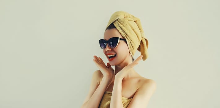 Portrait of stylish surprised laughing woman drying her wet hair with wrapped towel on her head having fun in trendy sunglasses on gray background