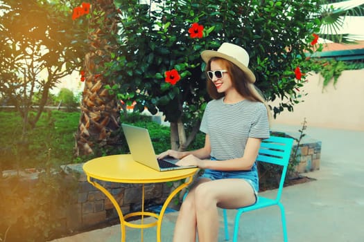 Happy young woman working with laptop sitting at the table in street cafe in summer park