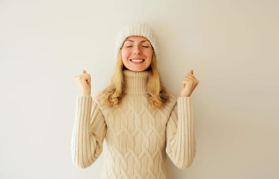 Overjoyed happy woman doing winner gesture celebrate clenching fists say yes expressing emotions of joy and victory win in knitted sweater and hat