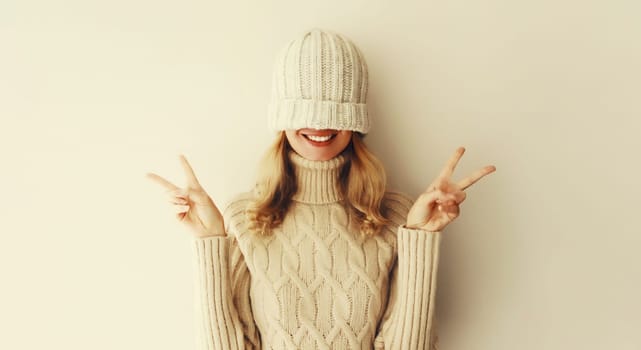 Cheerful funny woman having fun, pulling winter hat over her face and covering her eyes in warm soft knitted clothes, sweater