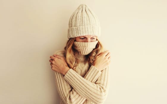 Woman freezing trying to warm up in winter warm knitted clothes, hat and sweater at home