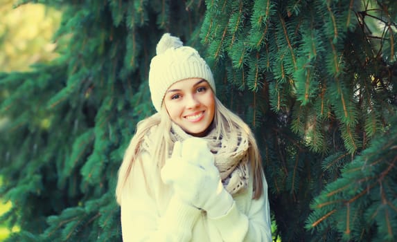 Winter portrait of happy smiling young woman wearing hat, knitted sweater and scarf in forest on christmas tree background