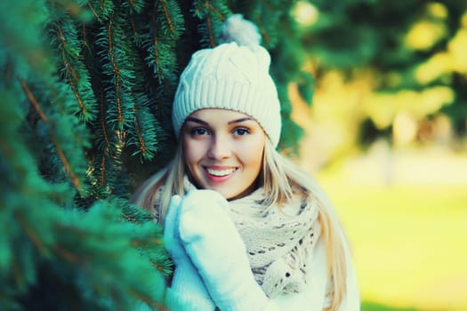 Winter portrait of happy smiling young woman wearing hat, knitted sweater and scarf in forest on christmas tree background