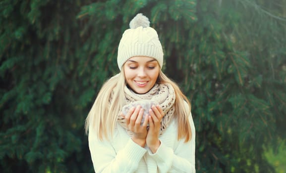Winter portrait of happy woman warms up holds mug of hot coffee in hat, scarf in forest on christmas tree background