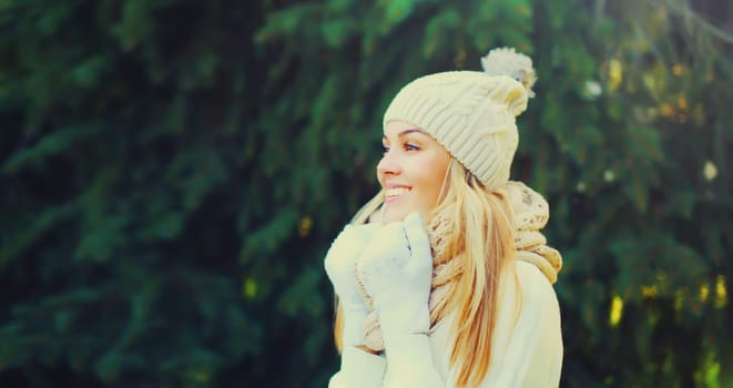 Winter portrait of happy smiling young woman wearing hat, knitted sweater and scarf in forest on christmas tree background