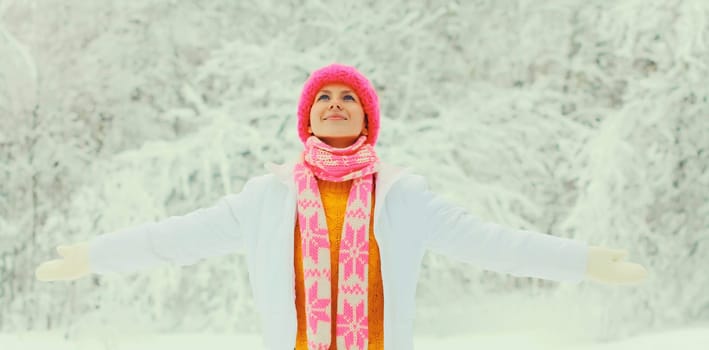 Winter portrait of happy smiling young woman in colorful knitted hat, scarf enjoys weather on snowy forest park background