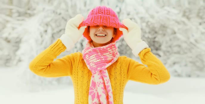 Winter portrait of happy cheerful smiling young woman having fun in colorful knitted hat, scarf enjoys weather in snowy park