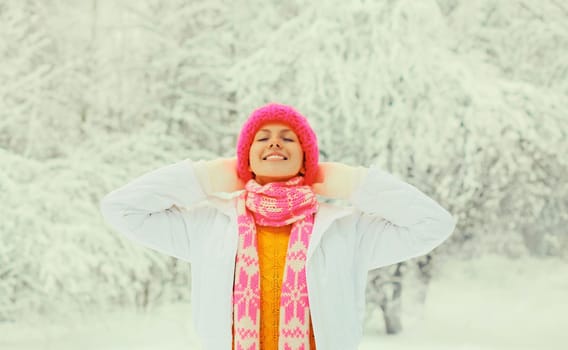 Winter portrait of happy smiling young woman in colorful knitted hat, scarf enjoys weather on snowy forest park background