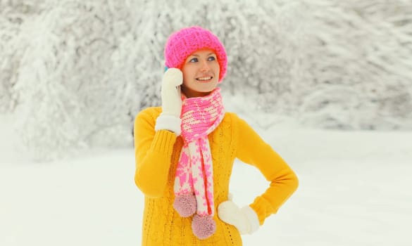 Happy young woman calling on smartphone looking away in colorful knitted hat, scarf and sweater in snowy park