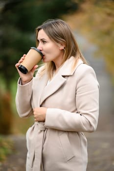 A young girl in the autumn park drinks coffee, rest in the park.