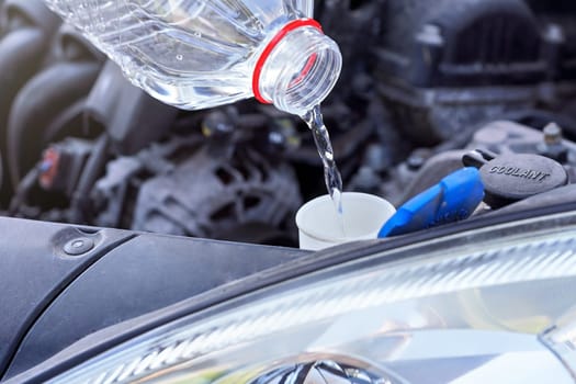 Pouring distilled water (ecological alternative to washing fluid) to washer tank in car, detail on clear plastic bottle
