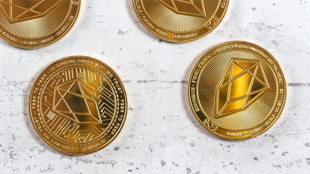 Golden commemorative EOS - EOSIO  cryptocurrency - coins on white stone board, overhead photo
