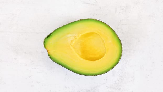 Avocado half, with bright yellow pulp on white stone board, photo from above
