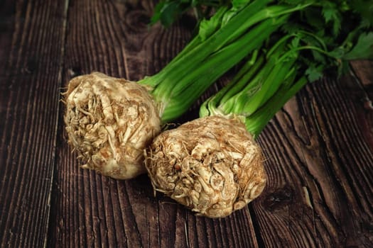 Celeriac roots with green leaves on dark wooden boards
