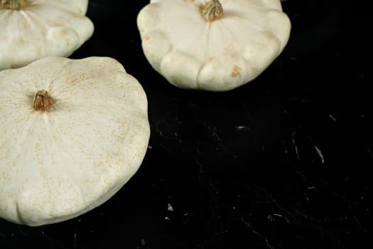 White pattypan squash heads on black marble like board, space for text right down corner
