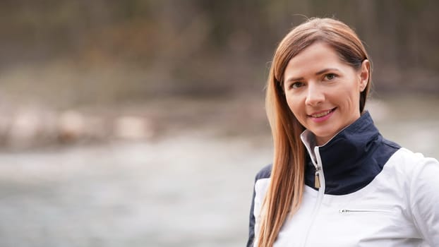 Portrait of young brunette woman in white jacket, blurred river (space for text) background