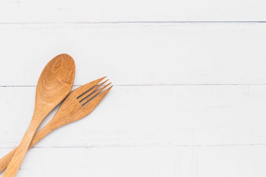 Wooden kitchen utensils including a spoon and fork on white table background with copy space