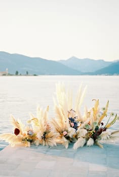 Bouquets of flowers stand on a pier by the sea against the backdrop of mountains. High quality photo