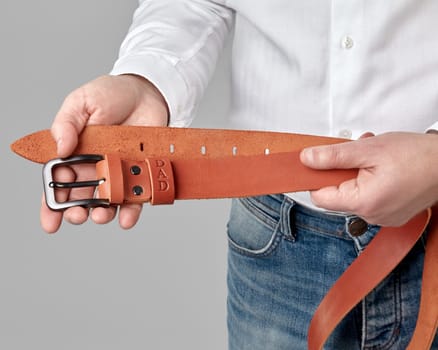 Closeup of stylish handcrafted copper-colored genuine leather belt with DAD embossing on loop in male hands, combining individual style with artisanal quality