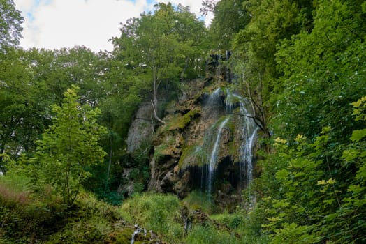 Waterfall Bad Urach at Southern Germany Longexposure. Cascade panorama in Bad Urach Germany is a popular natural attraction and waterfall sight called Uracher Wasserfall . Natural reserve in autumn season with colorful foliage and longtime exposure. Panoramic view of Bruehlbach creek or brook with cascade in Bad Urach, Germany near waterfall sight Uracher Wasserfall . Natural reserve on a summer morning after heavy rain in lush forest.