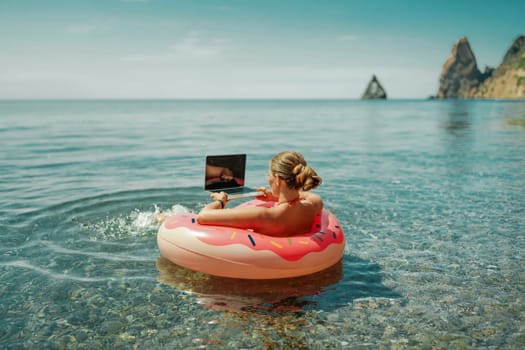 Woman laptop sea. Freelancer woman in sunglases floating on an inflatable big pink donut with a laptop in the sea. People summer vacation rest lifestyle concept