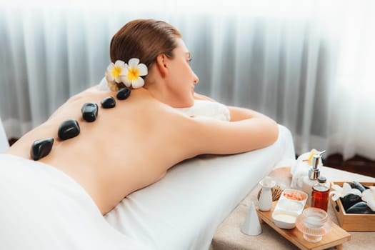 Hot stone massage at spa salon in luxury resort with day light serenity ambient, blissful woman customer enjoying spa basalt stone massage glide over body with soothing warmth. Quiescent