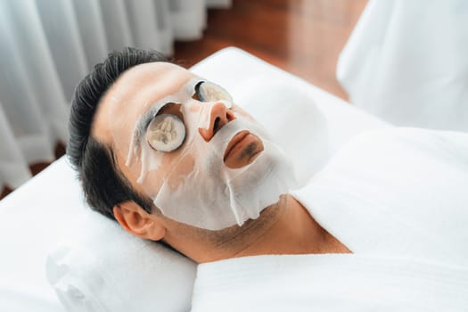 Serene daylight ambiance of spa salon, man customer indulges in rejuvenating with luxurious cucumber facial mask. Facial skincare treatment and beauty care concept. Quiescent