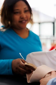 African american woman holding multiple shirts, buying stylish clothes in modern boutique. Smiling shopper wanting new wardrobe, shopping for fashionable merchandise and accessories