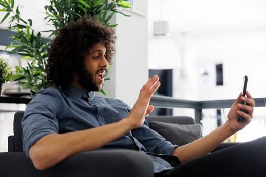 Cheerful arab entrepreneur greeting coworker while having online communication on smartphone. Happy executive manager discussing project on mobile phone videocall in start up business office