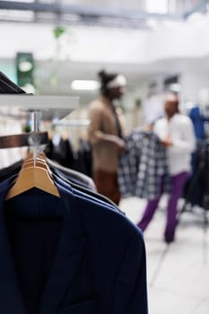 Male shirts hanging on rack for sale in retail shopping mall with blurred background. Casual trendy menswear apparel on hangers in fashion boutique close up selective focus