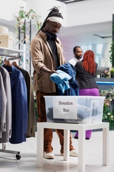 African american man donating old clothes to charity organization in shopping mall. Fashion boutique customer putting formal clothes in container for welfare to help poor