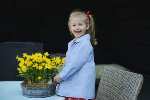 A girl in a dress near a pot of daffodils