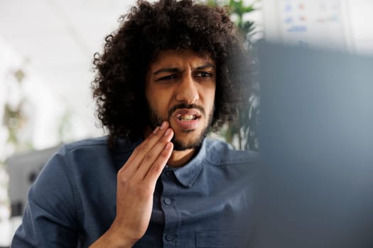 Young arab employee with toothache having online chat with dentist at workplace. Entrepreneur with tooth pain calling doctor on laptop while working in business company office