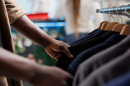 African american man browsing jackets on rack while choosing formal menswear in clothing store. Buyer hands searching for stylish blazer hanging in shopping mall fashion boutique